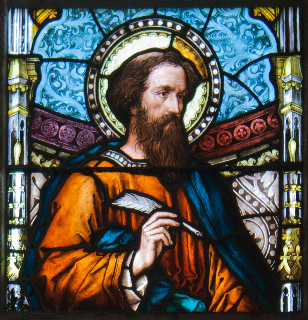 Stained glass window of St Luke the Evangelist holding a quill